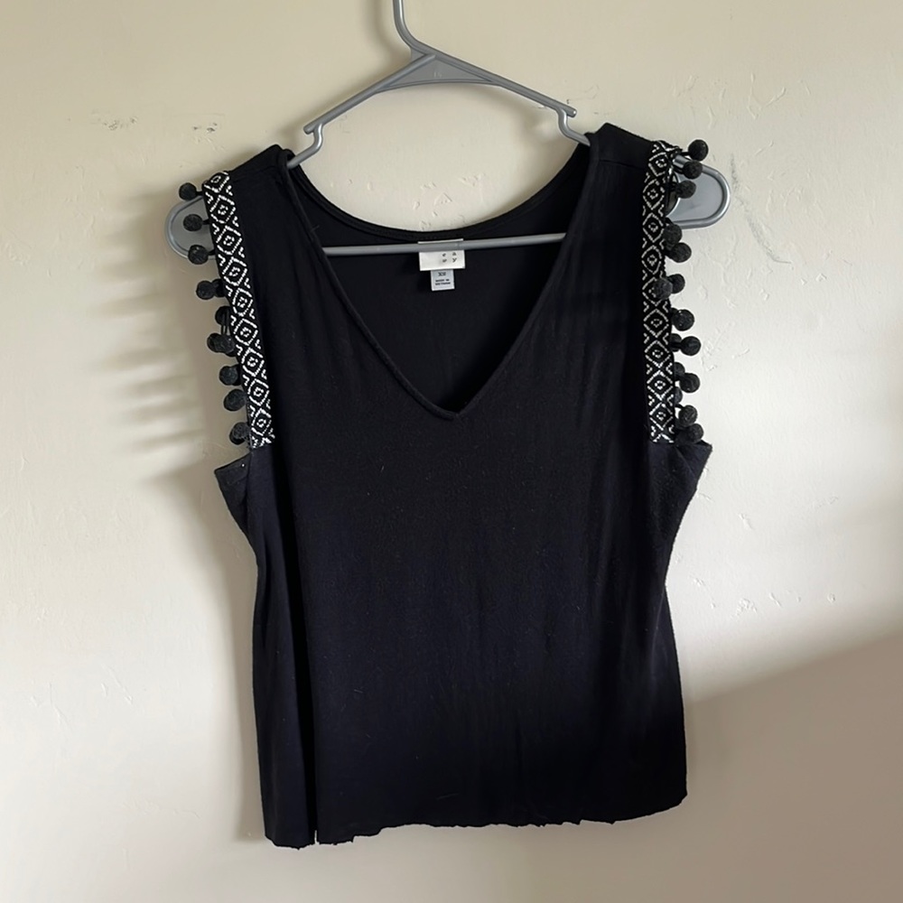 Black tanktop with pom-poms on the sleeves.